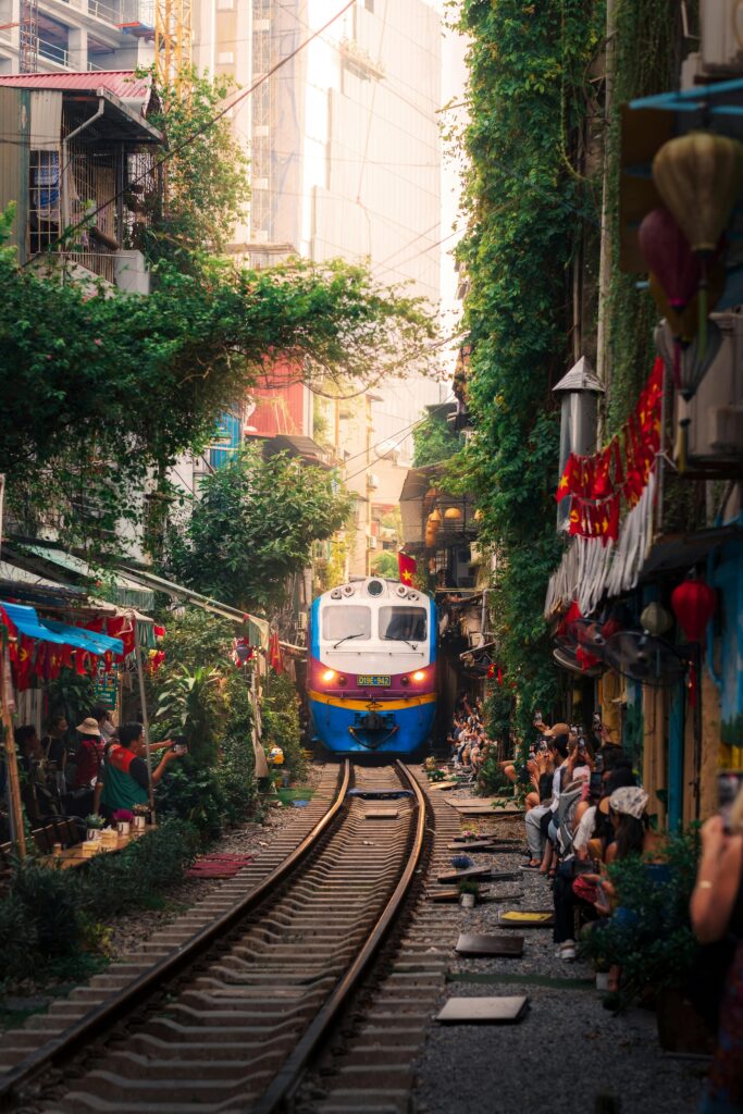 Train navigating through Hanoi's iconic street with vibrant surroundings and local life.