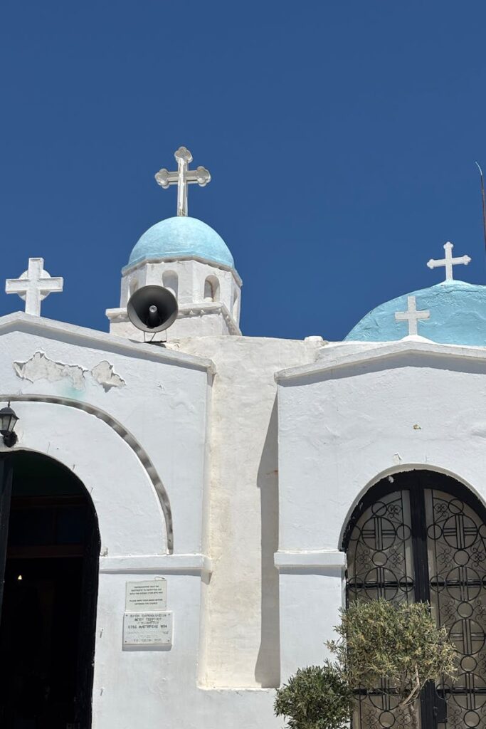 Beautiful whitewashed Orthodox church in Athens with blue domes under clear sky.