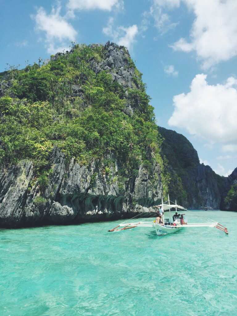 A breathtaking view of El Nido, Philippines with a boat sailing past towering cliffs and turquoise waters.